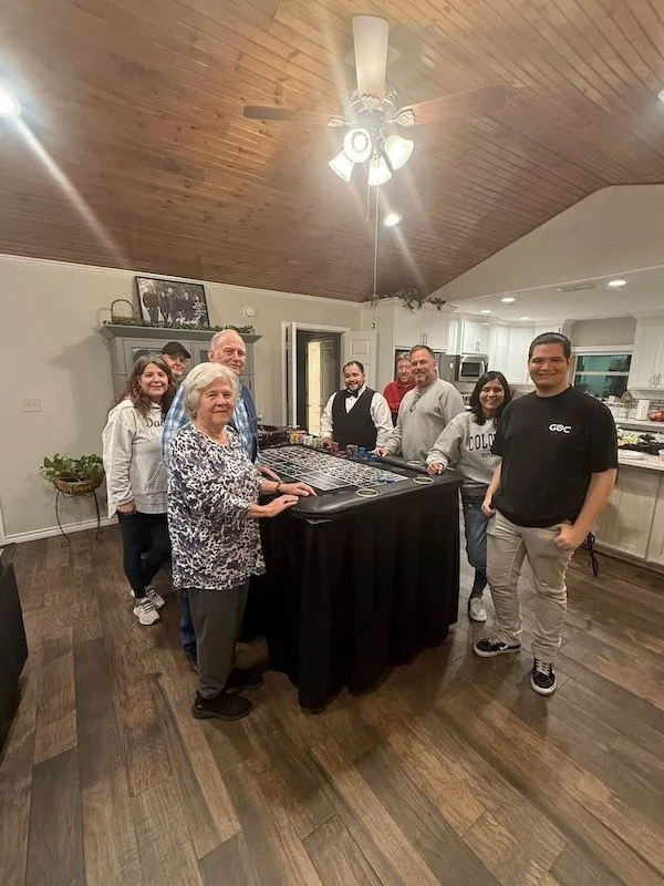 A small group of people smiling at the camera surrounding a casino style game table in their household