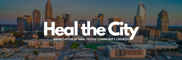 A city skyline at sunset with tall buildings and skyscrapers, featuring a church or community center sign that reads 'Heal the City,' indicating an initiative by Heal House Community Church.