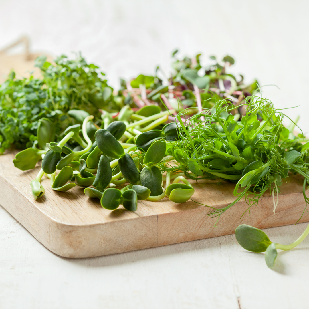 Assorted fresh microgreens on a wooden cutting board.