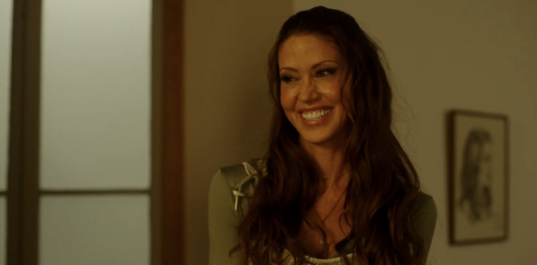 A woman with long, wavy hair smiling in an indoor setting.