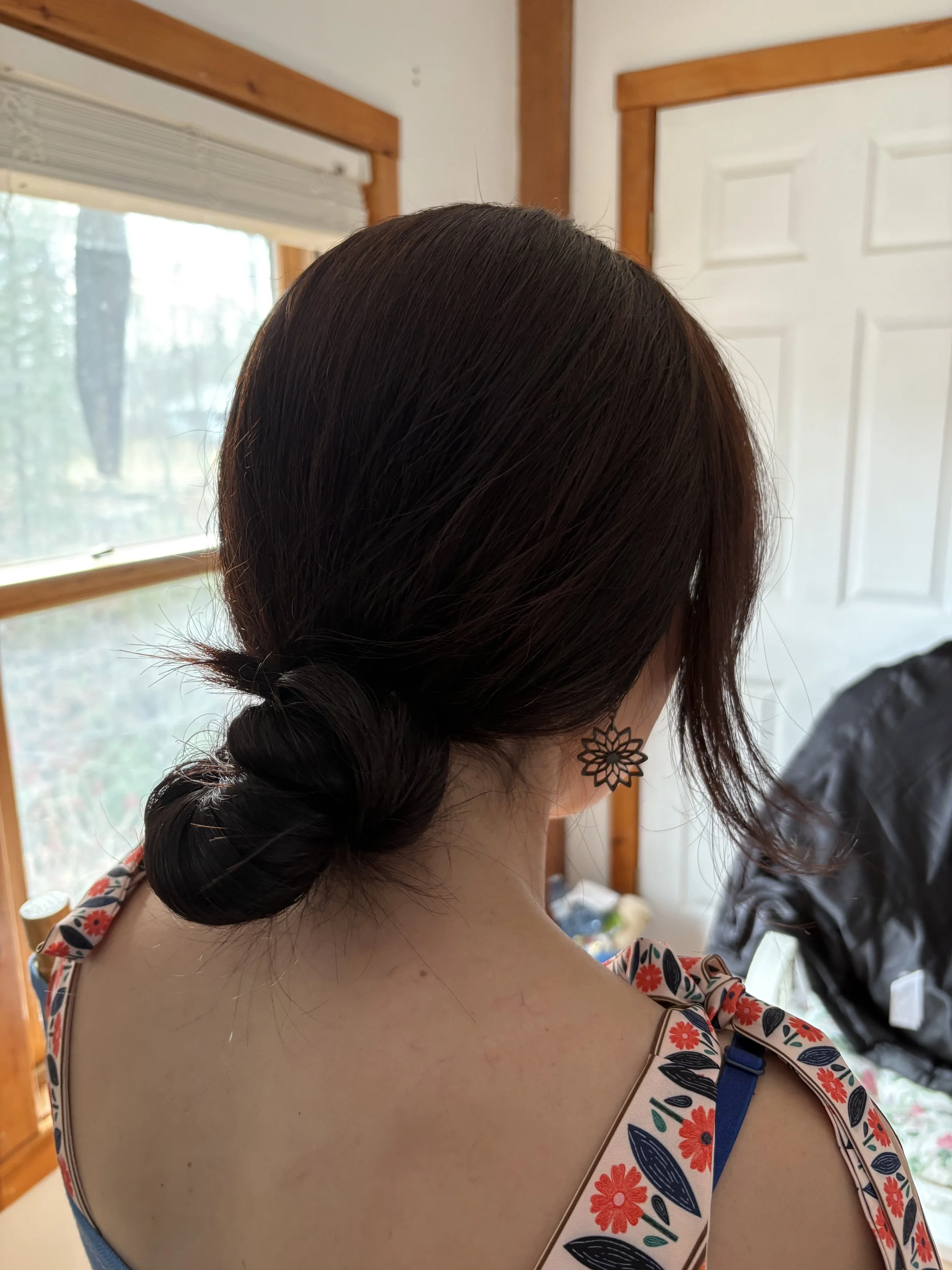 Back of a woman with dark hair in a twisted bun wearing floral earrings and a sleeveless top with a floral pattern.