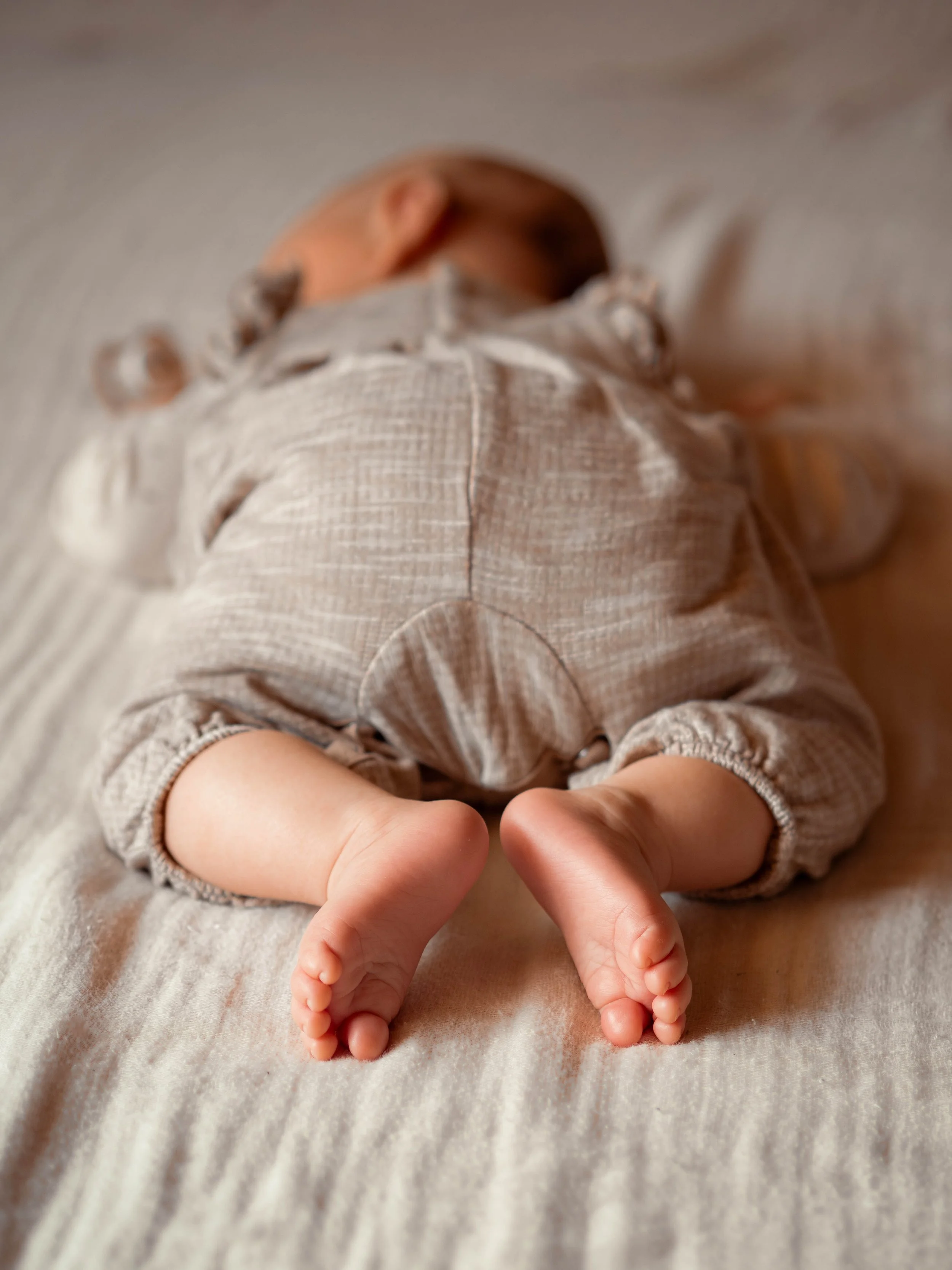 Ein Baby liegt auf dem Bauch auf einem weißen Stoff, die nackten Füße sind sichtbar.