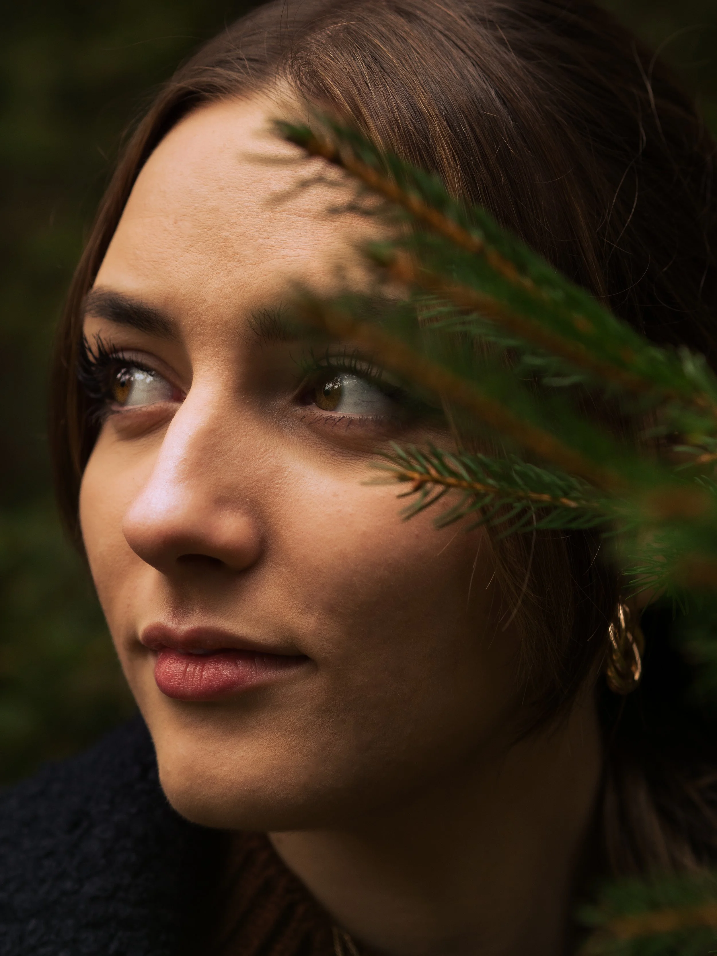 Nahaufnahme des Gesichts einer Frau, die nach oben schaut, mit braunen Haaren und braunen Augen, teilweise verdeckt durch ein grünes Blätterblatt.