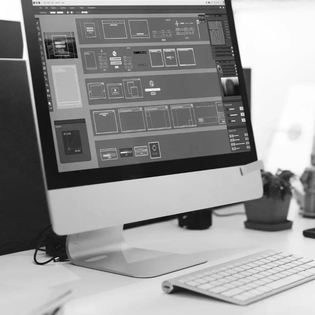 Schwarzer und weißer Desktop-Computer mit einem Monitor, auf dem Design- oder Bearbeitungssoftware geöffnet ist, neben einer kabellosen Tastatur auf einem weißen Schreibtisch