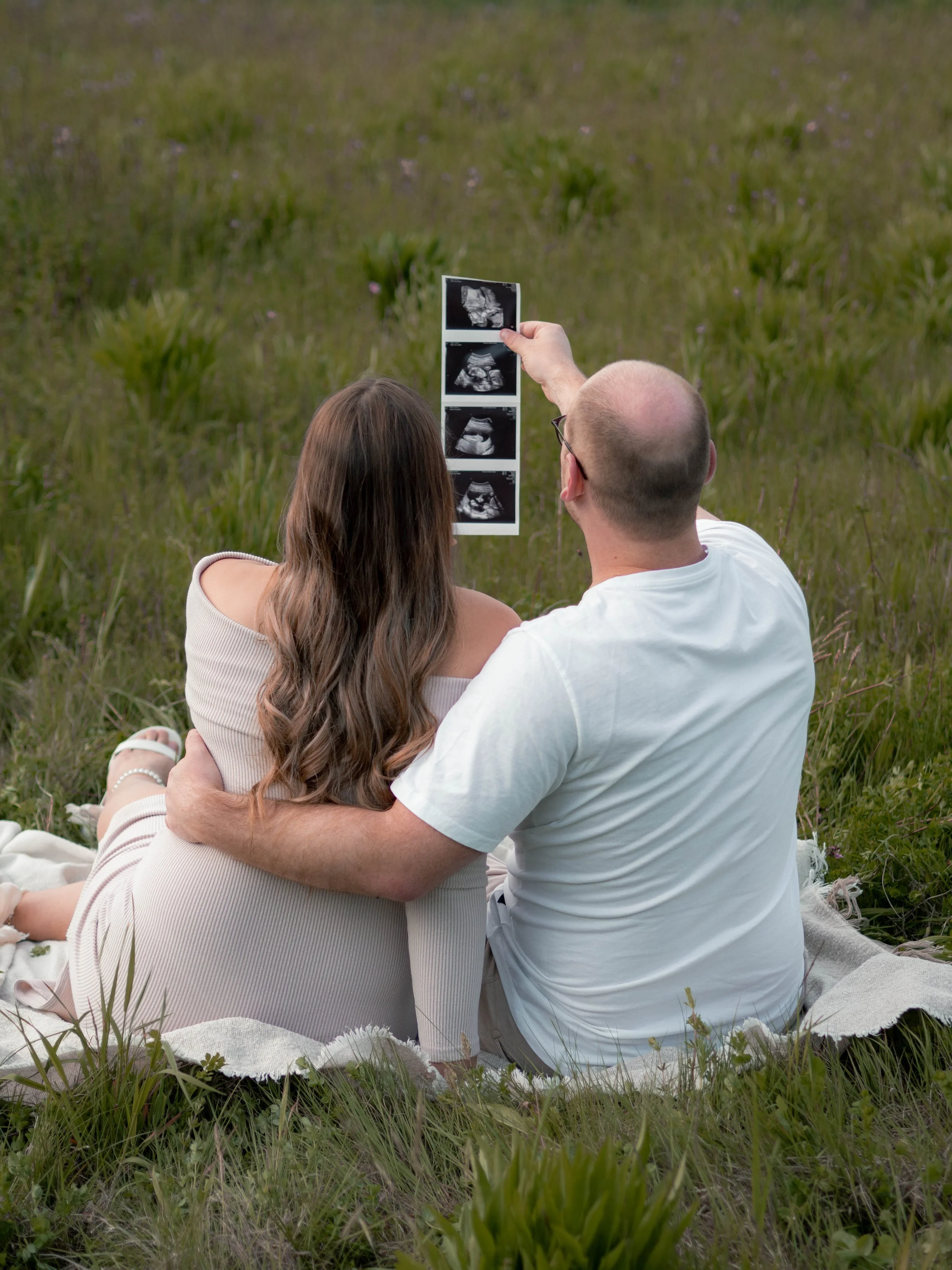 Ein Paar sitzt auf einer Wiese und schaut auf Ultraschallbilder, vermutlich eines Babys.