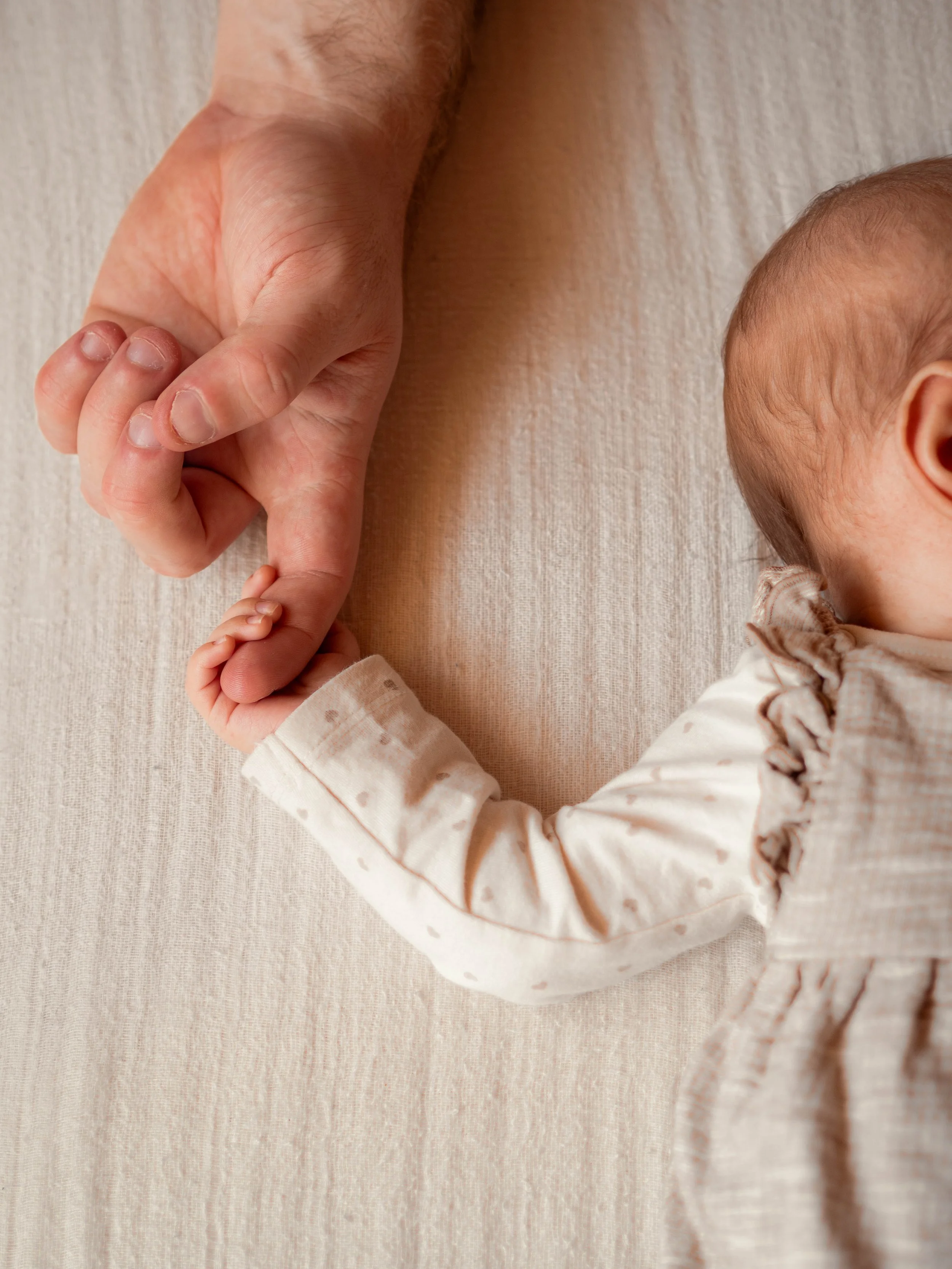 Ein Baby hält den Finger eines Erwachsenen. Der Hintergrund ist ein helles, strukturierte Gewebe.