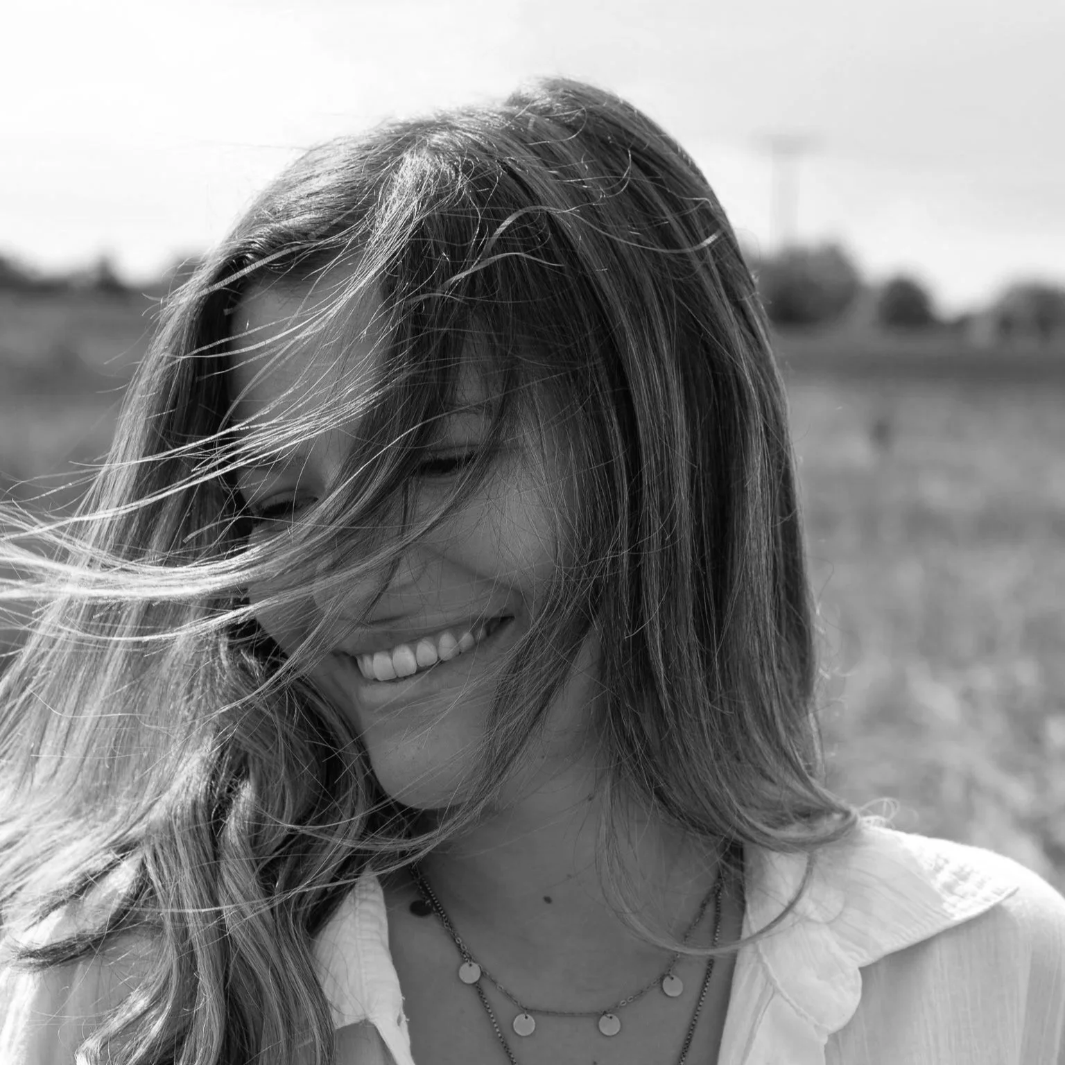 Junge Frau mit langen Haaren, lachend im Freien, Wind weht durch die Haare, in schwarzer und weißer Fotografie.
