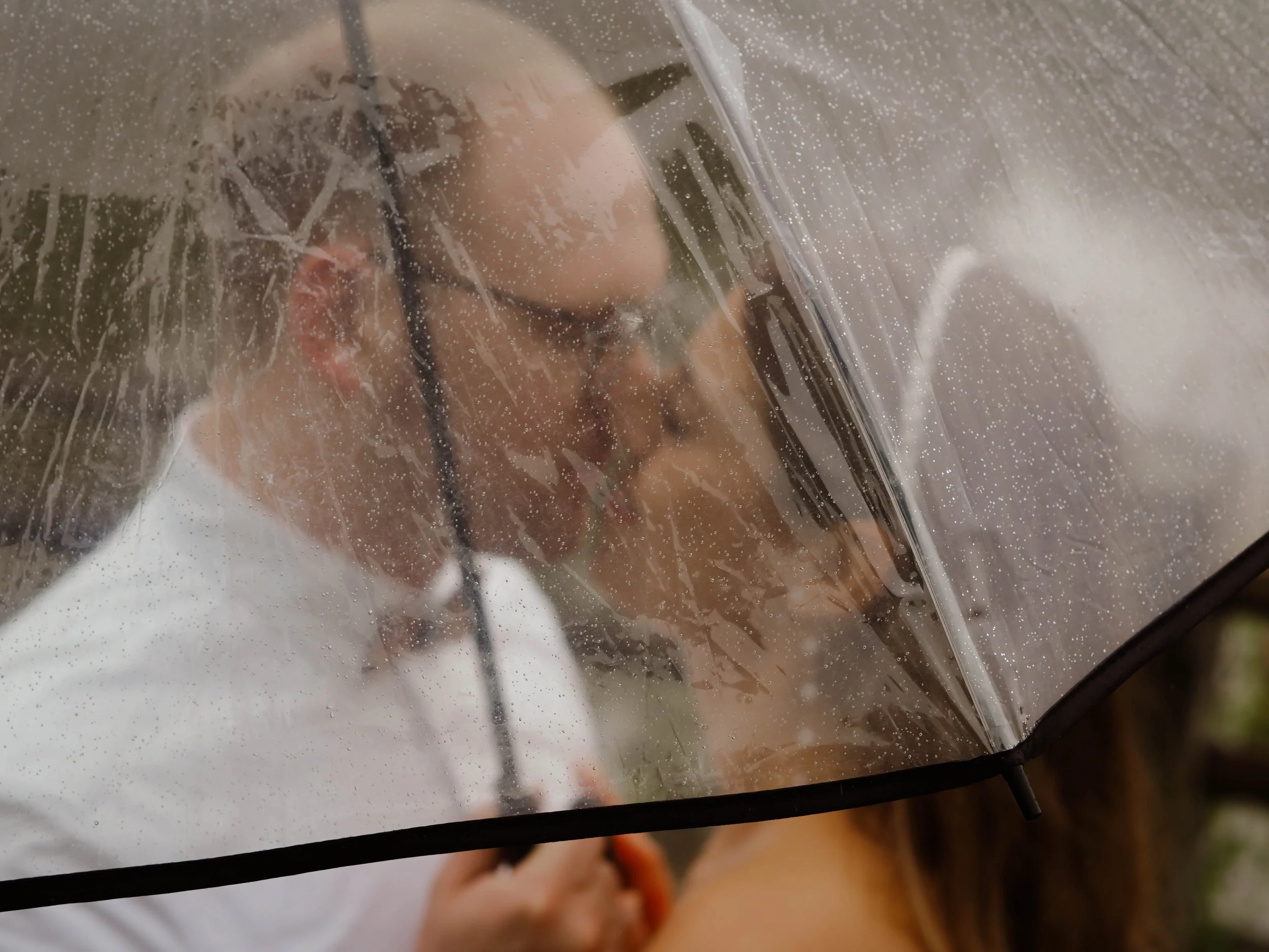 Ein Hochzeitspaar küsst sich unter einem Regenschirm. Das Bild wurde durch den durchsichtigen Schirm fotografiert.