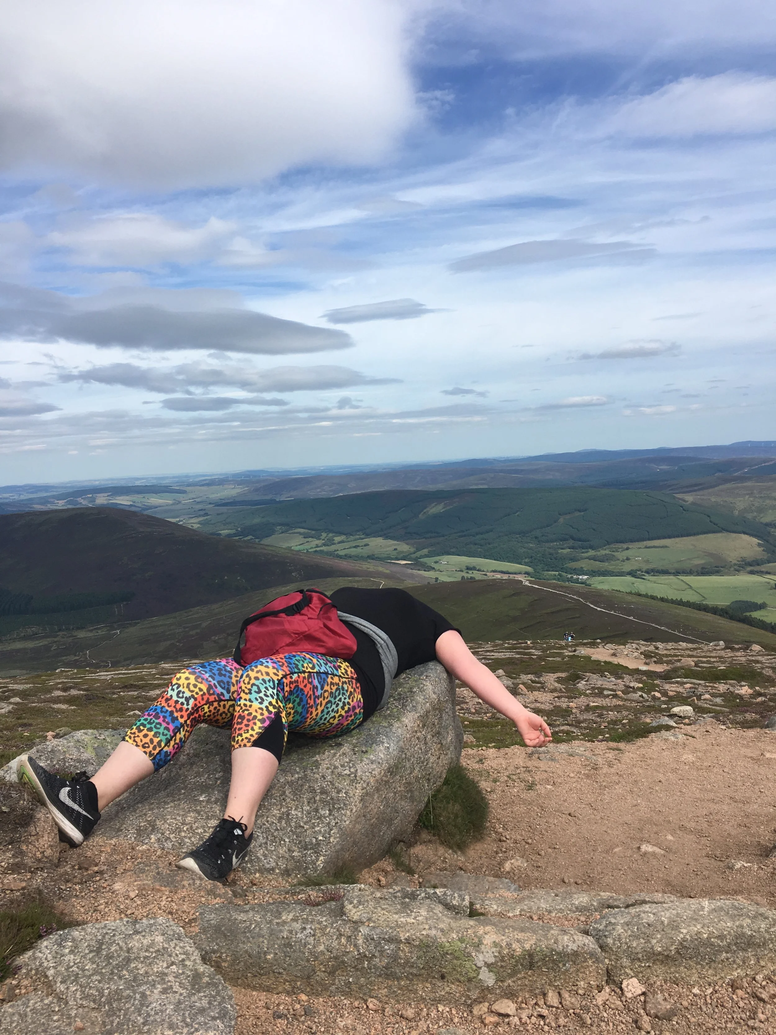 Picture of a woman in sports clothing lying on rock halfway up a big hill.