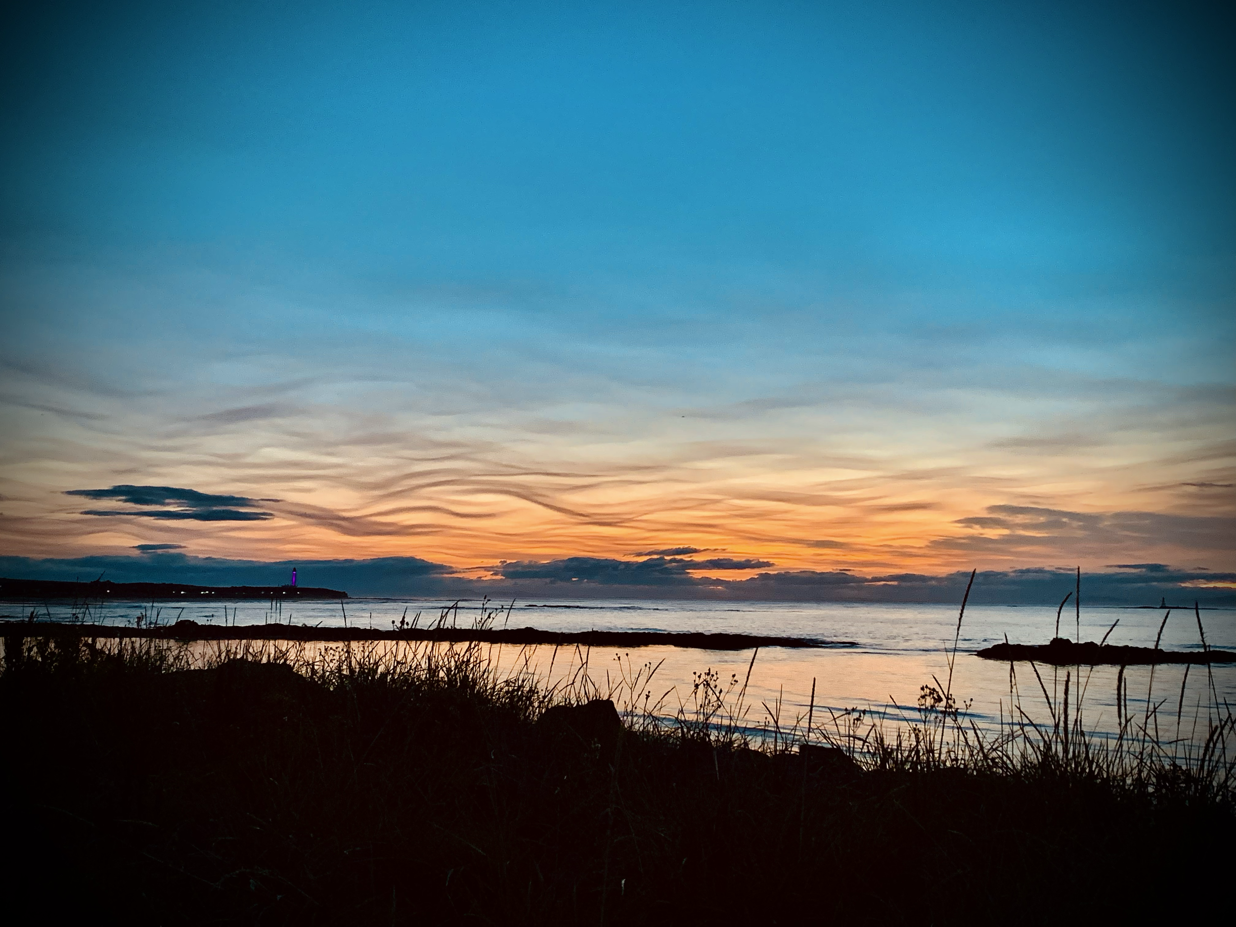 Photo of a sunset with blue orange and yellow and siwrly clouds