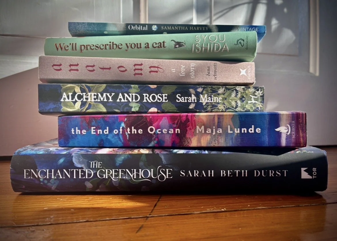 Image of a stack of books: Orbital, We'll Prescribe you a cat, Anatomu, Alchemy & Rose, The end of the ocean, and the enchanted Greenhouse