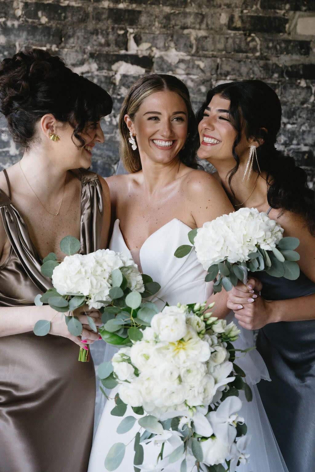 A bride and her bridesmaids on the wedding day. They are all holding bouquets with white flowers and smiling.