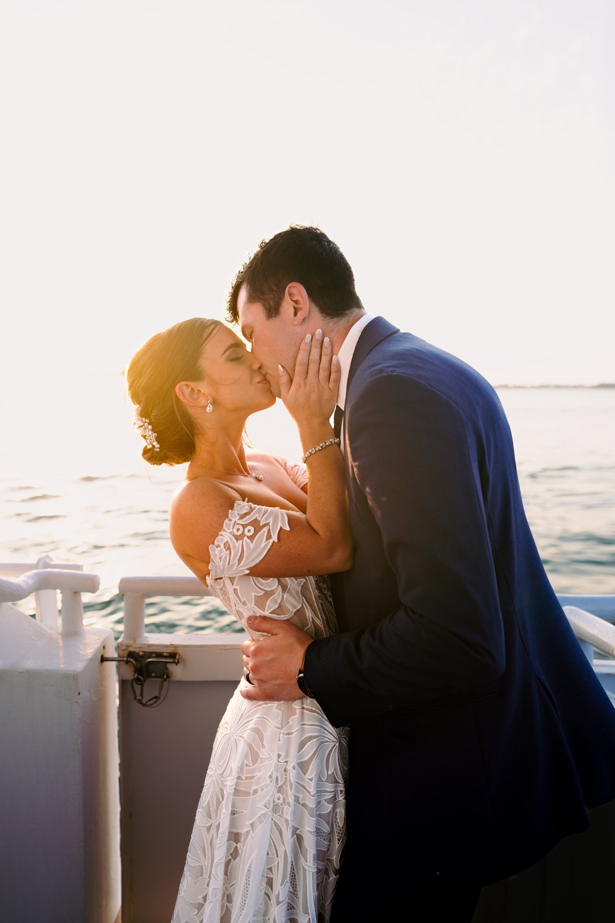 A couple in wedding attire sharing a kiss on a boat at sunset