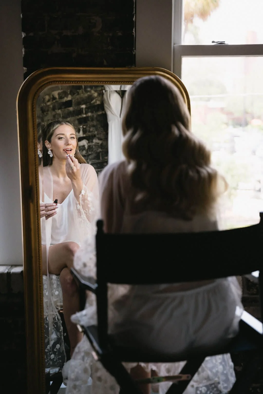 Bride applying lipstick in mirror while getting ready for her wedding.