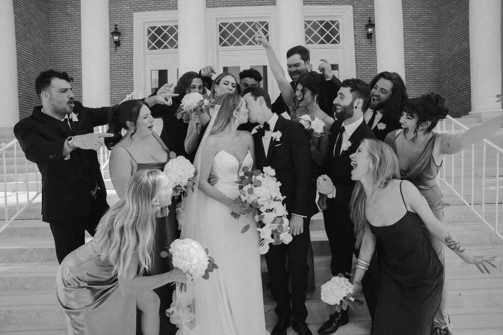 Wedding party celebrating with bride and groom on building steps.