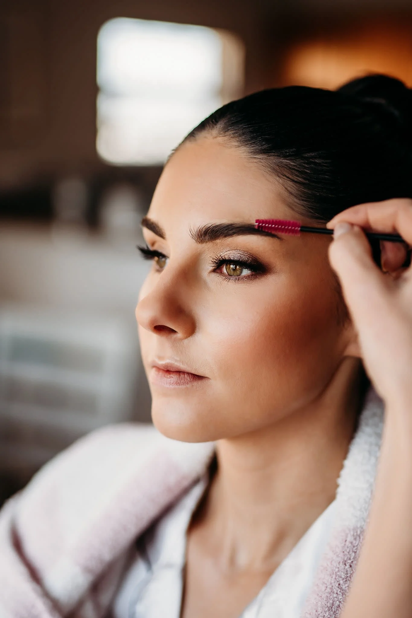 Close-up of a woman with dark hair pulled back, having makeup applied to her eyes.