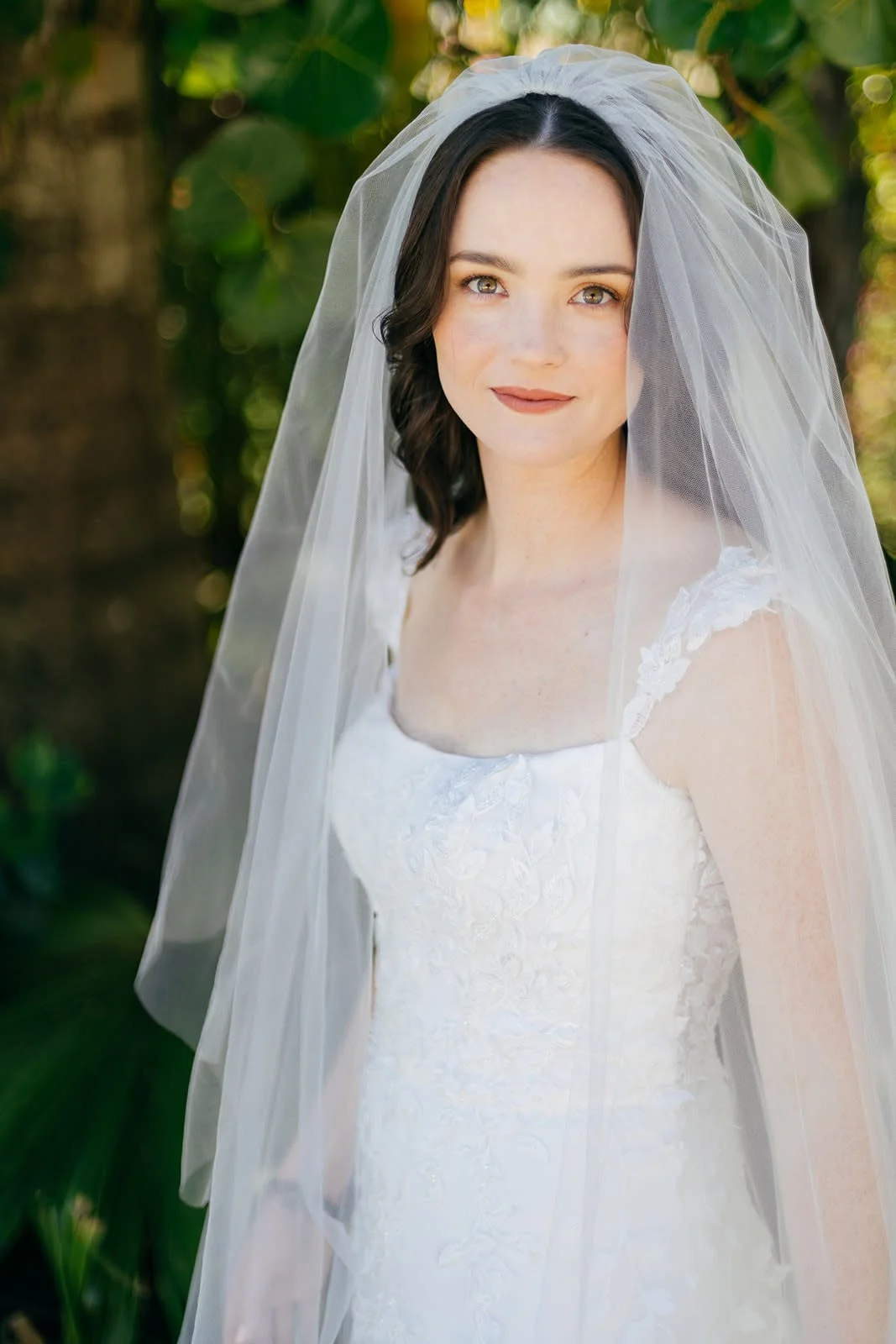 A bride with dark wavy hair and light eyes wearing a white wedding dress and veil.
