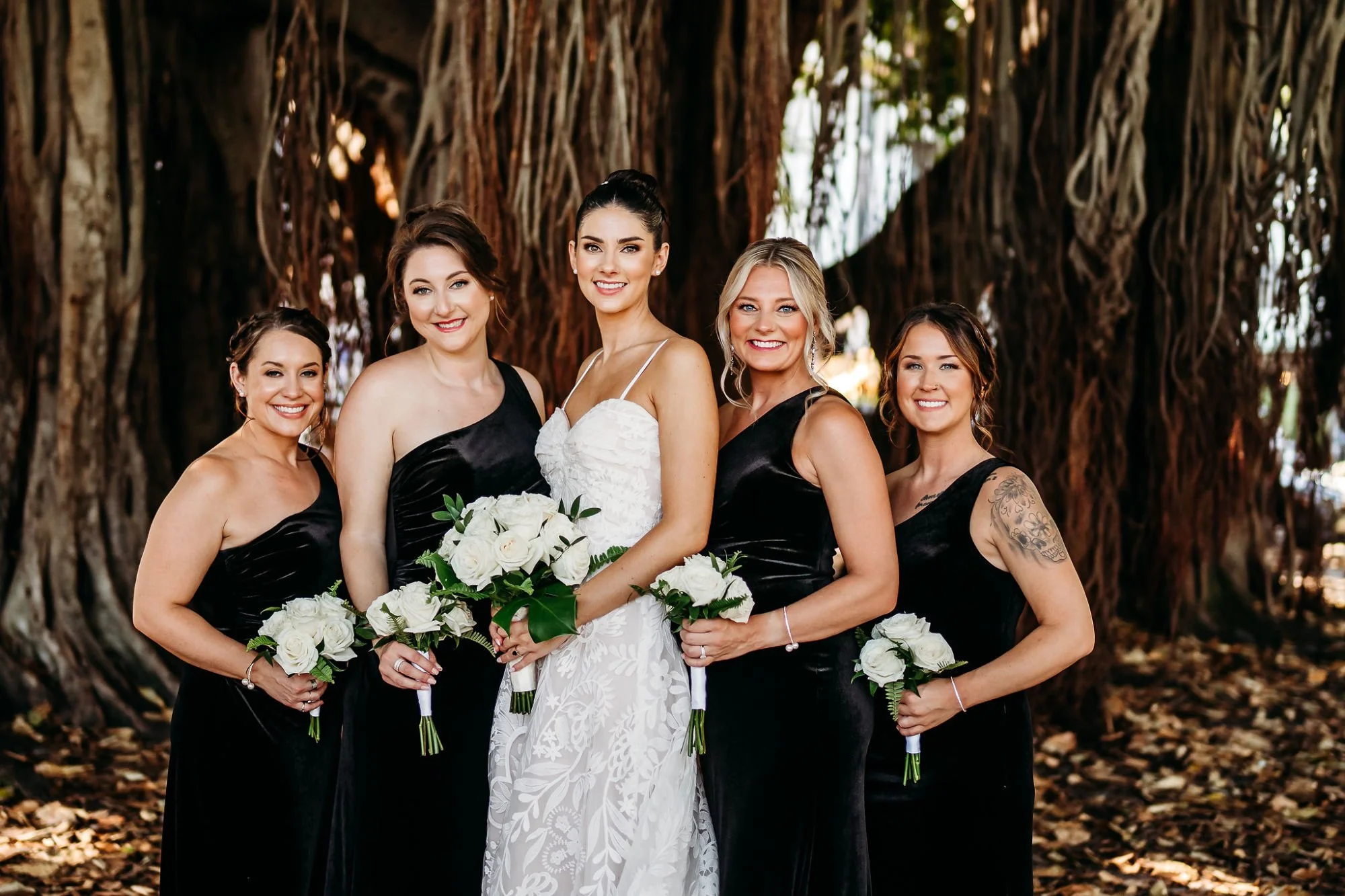 Bride and her bridesmaids holding bouquets and smiling in the woods.