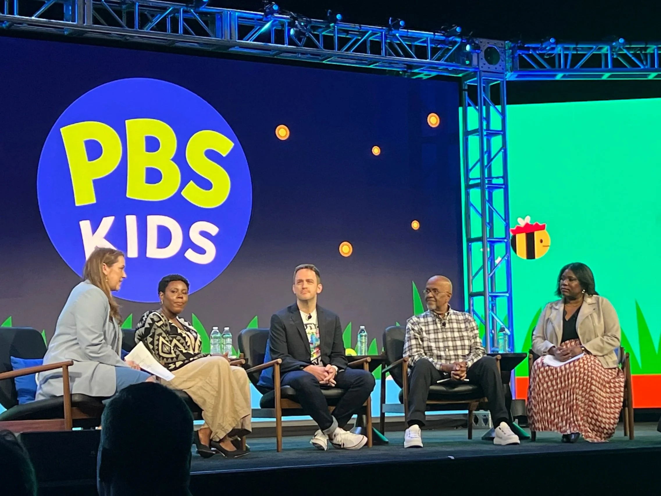 A panel discussion at a PBS Kids event with six speakers seated on stage for Lyla in the Loop, with a large PBS Kids logo and colorful decorations in the background.