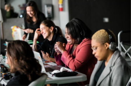 Veronica directing a video shoot on set with a diverse group of women working together smiling and engaging in discussion.