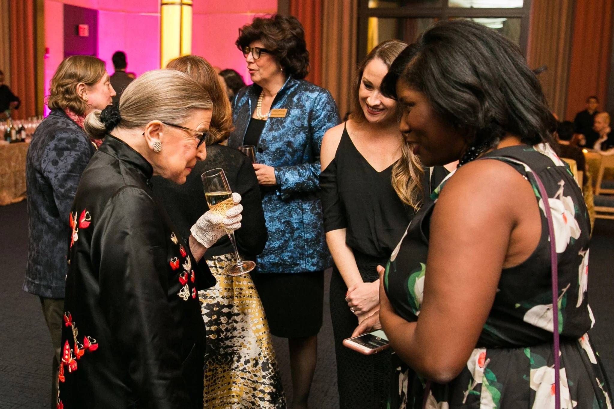 Ruth Bader Ginsburg at a social gathering talking and smiling with Veronica Toney in a brightly lit venue with warm colors.