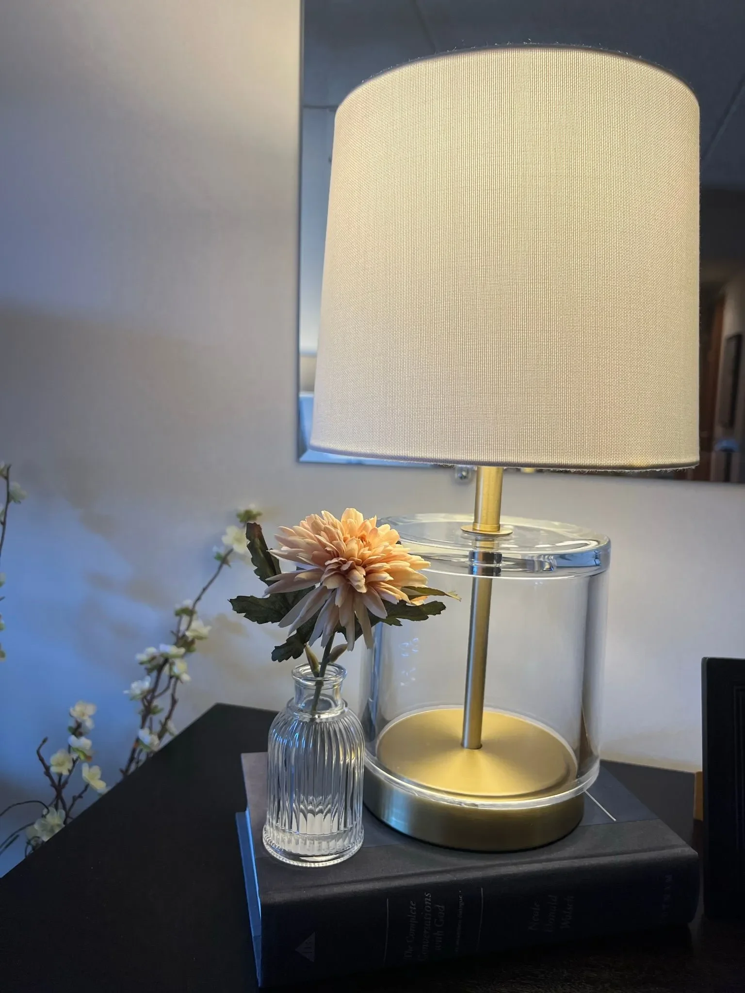 Side table with a modern, gold lamp and white lamp shade and a small vase with a flower in int