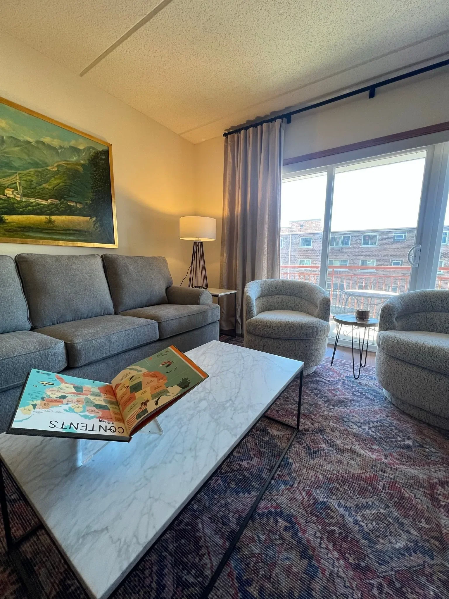 View of the living room with the couch and two comfortable chairs. All in grey and modern styles  with the patterned run beneath