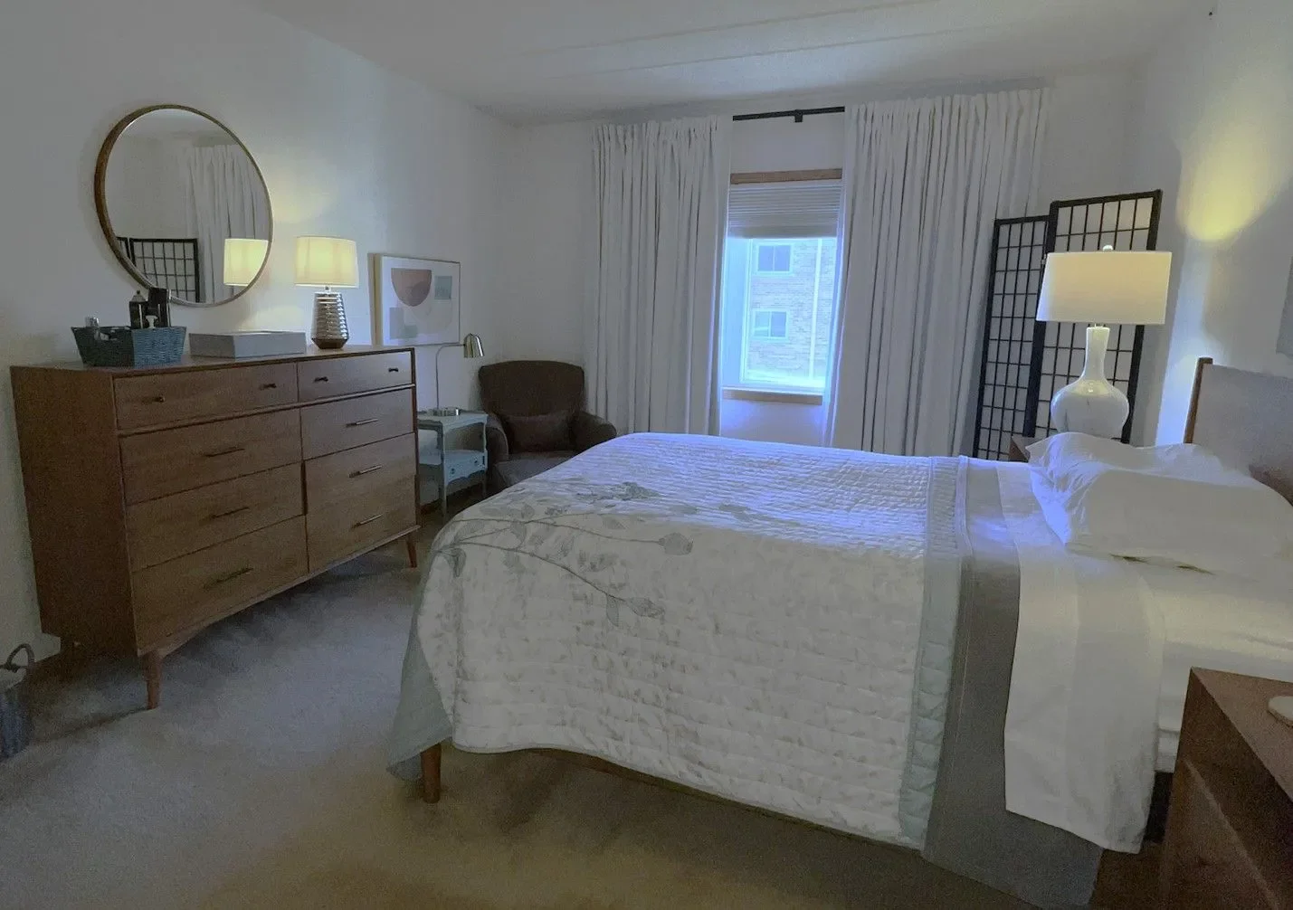 After image of the bedroom with updated and modern furniture, white curtains and warm art. 