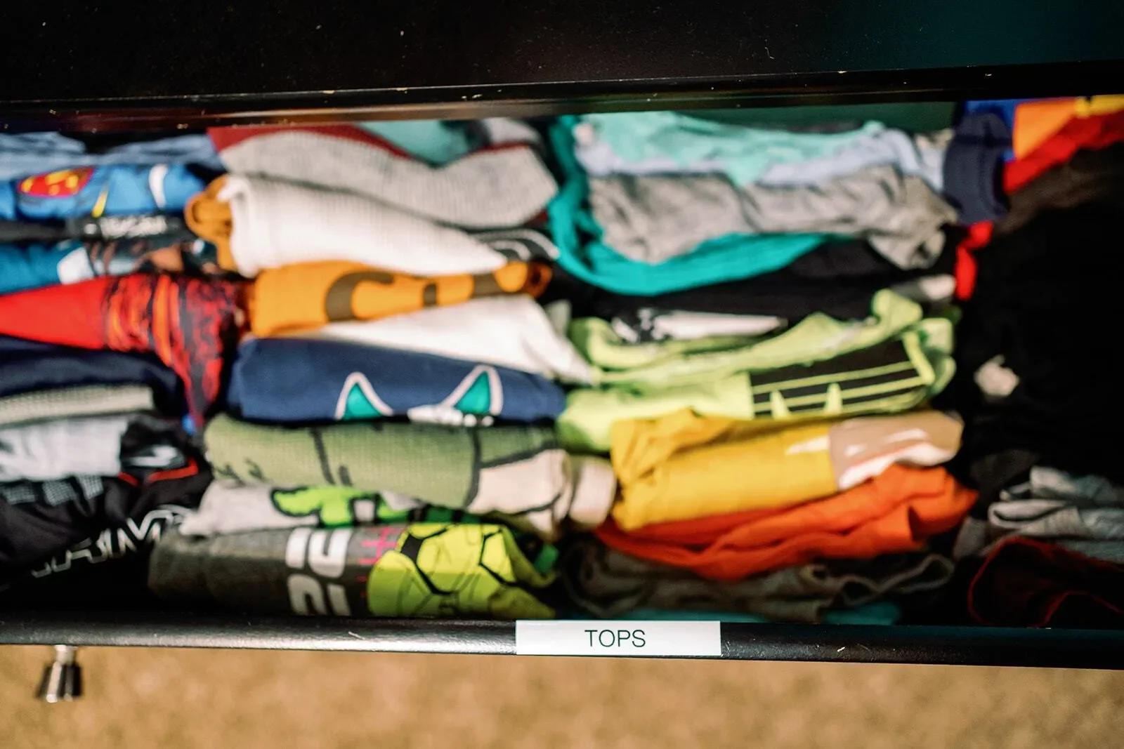 Kid's closet with properly folded tops and a label for the shelf titled tops