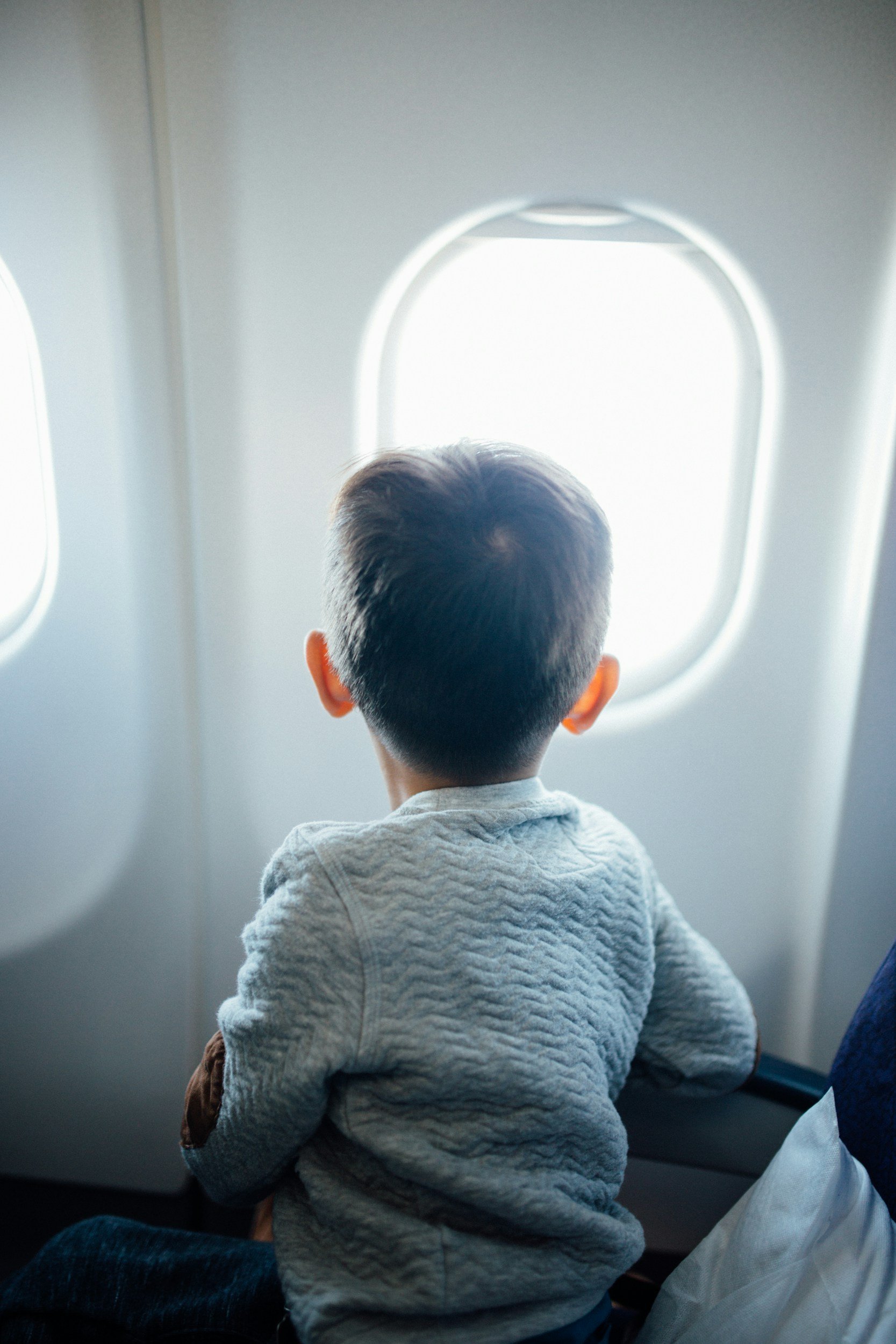 Image of a young boy looking out an airplane window with a grey sweater.