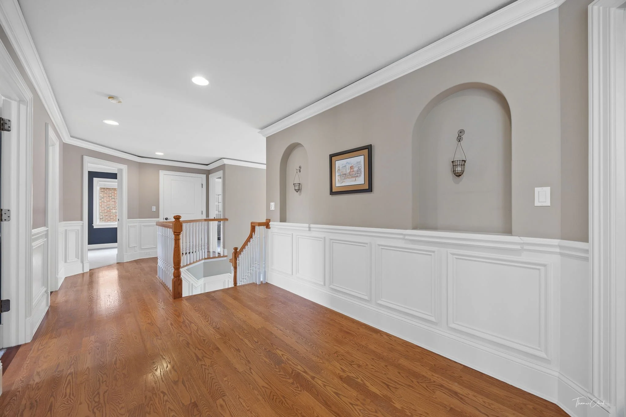 Open stairway landing staged with simple art. Wooden floors and white paneling.