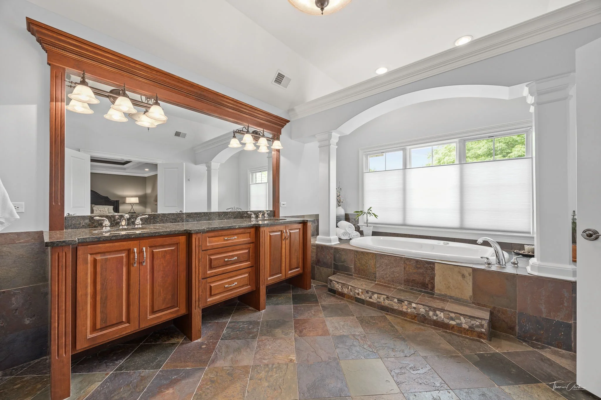 Master bathroom with a large window and darker wooden cabinets and stone bathtub