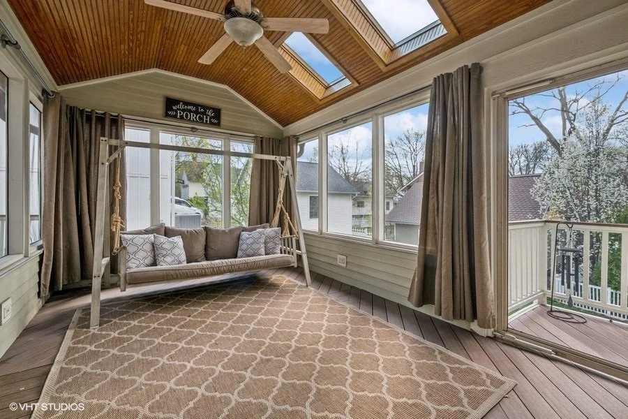 A bright sunroom staged with casual seating and greenery, emphasizing indoor-outdoor living.
