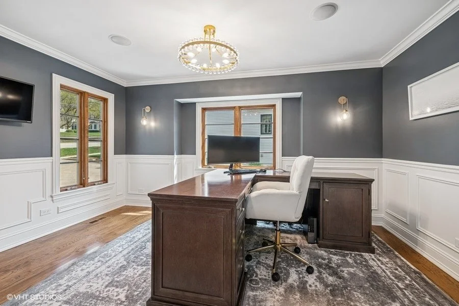 A professional home office staged with a sleek desk, a modern chair, and simple tabletop accessories near a window.