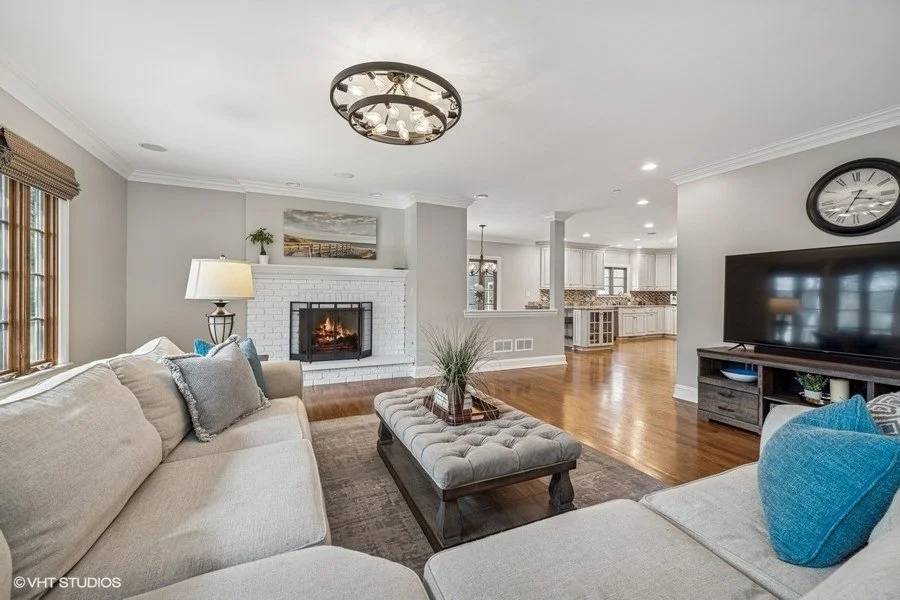Staged family room with light gray seating, a white area rug, and minimalist wall art, emphasizing a clean and open layout.