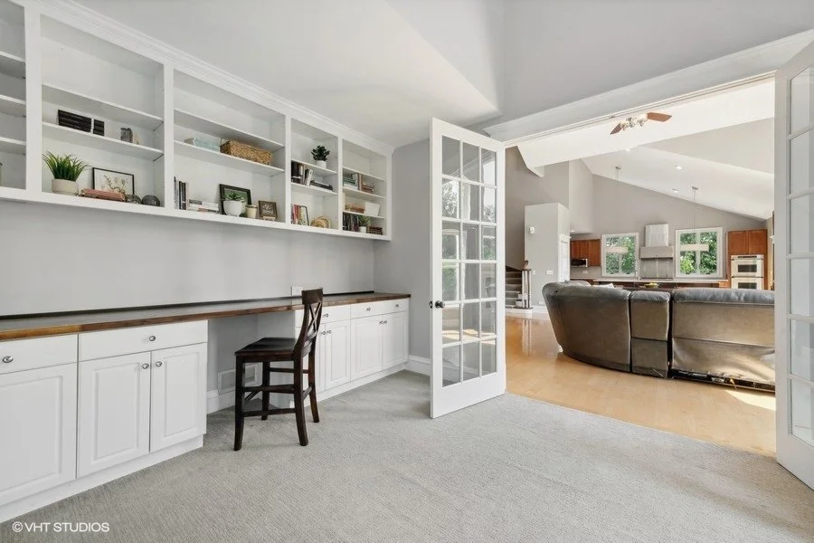 A bright home office staged with a large desk and a bookshelf with a simple chair. 