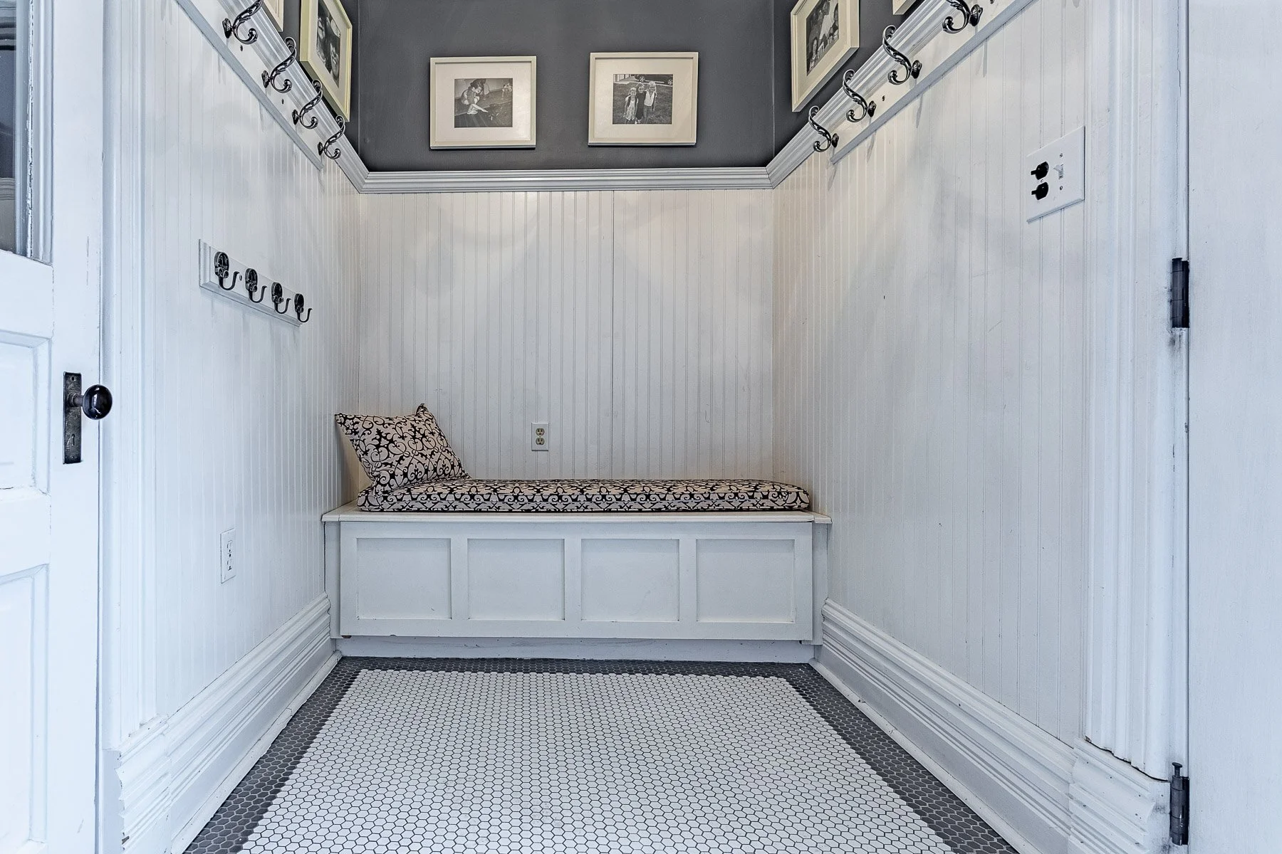 Staged mudroom with white paneling, a bench seating with a neutral throw pillow and white tiling