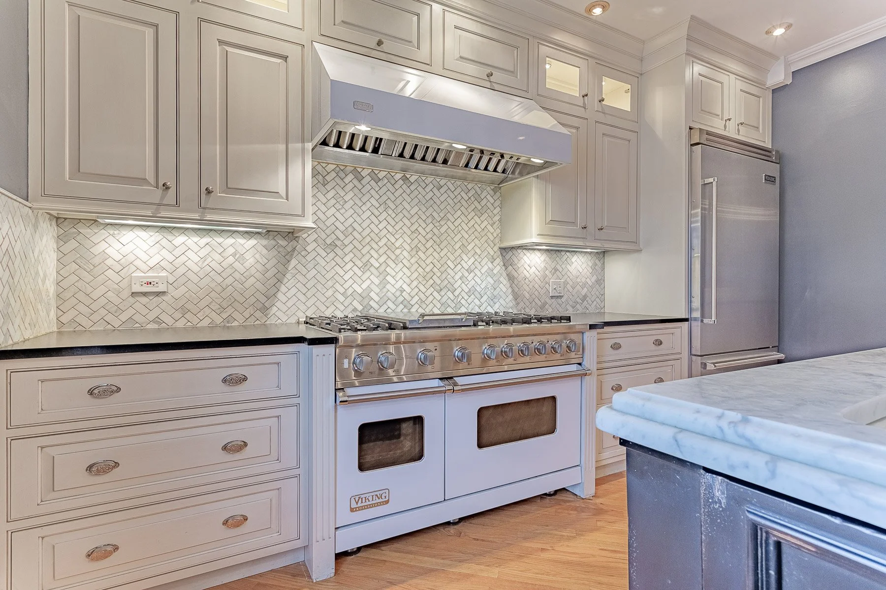A modern kitchen with a large range and white cabinets and wood floors