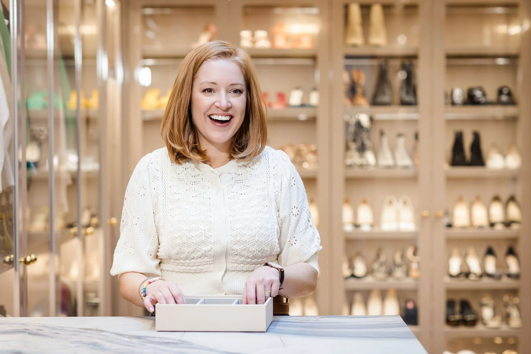 Ashley organizing a jewelry box in a luxury closet, wearing a white textured top and smiling