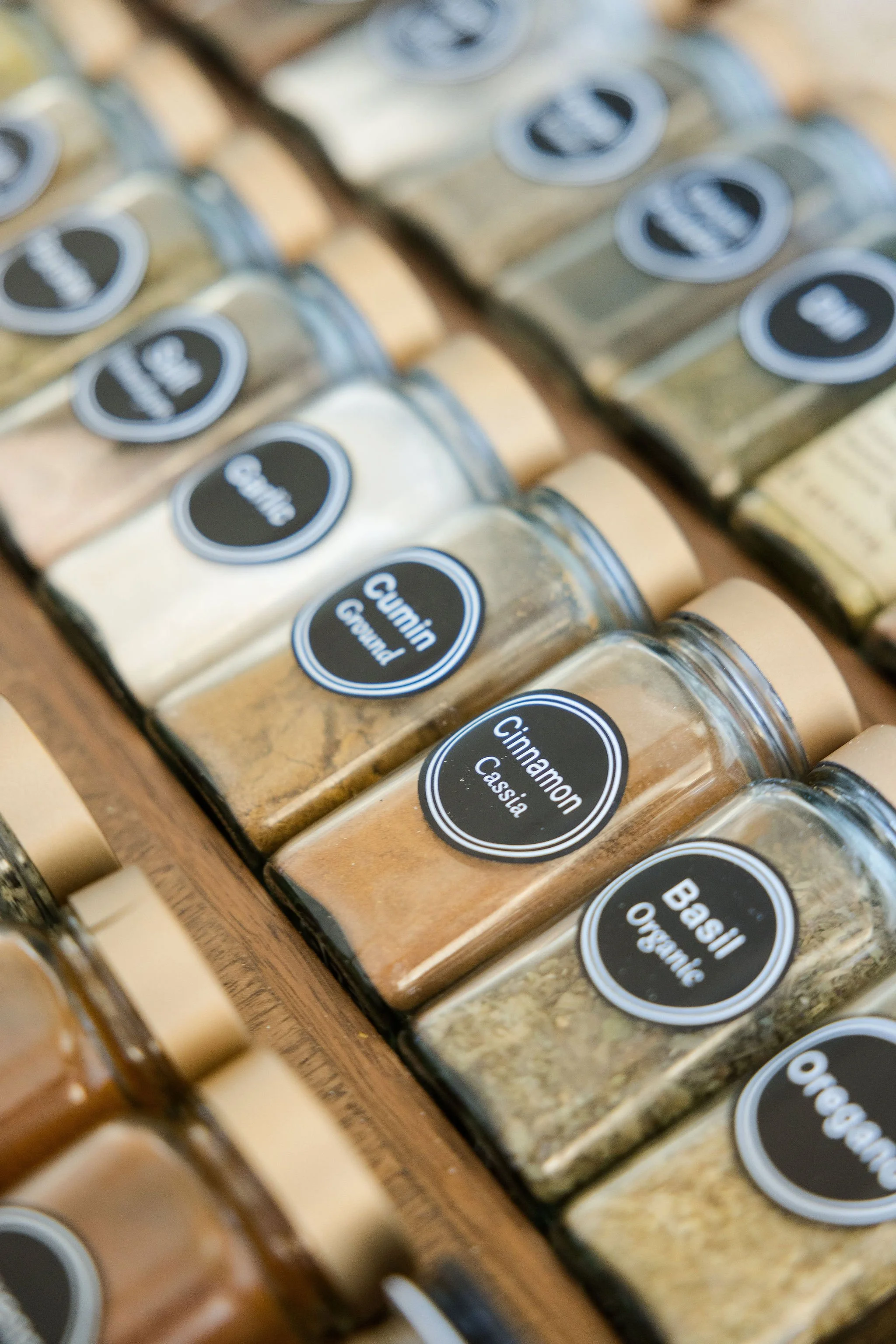 Close up of a spice drawer with rows of spices. Zoomed in on cinnamon, cumin and basil spices in separate glass jars