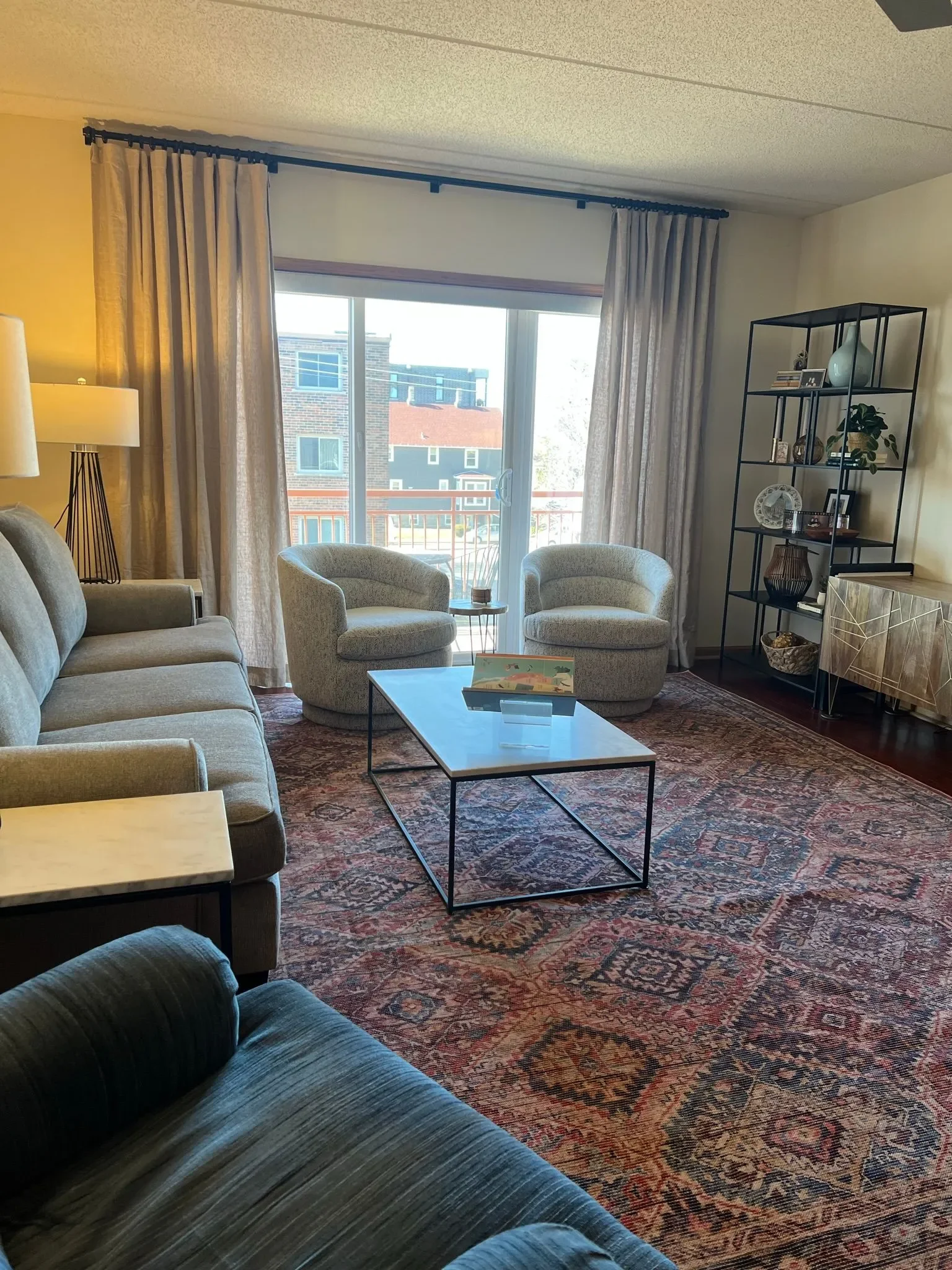 A "after" photo of the refreshed condo family room featuring a contemporary patterned area rug, a streamlined neutral sofa, and updated minimalist wall art.
