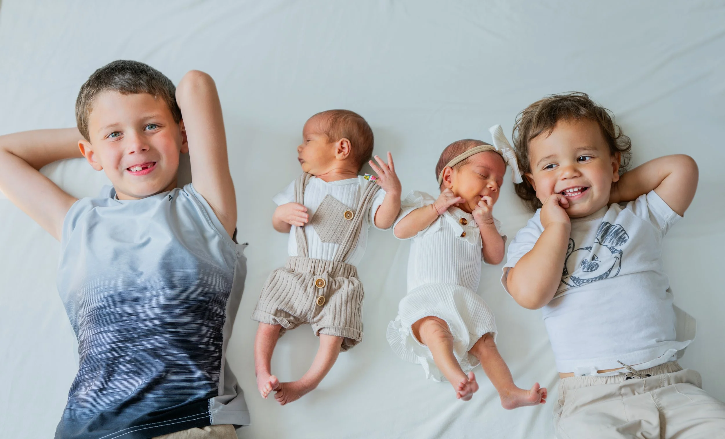 Four young children lying on a white surface, smiling and interacting.