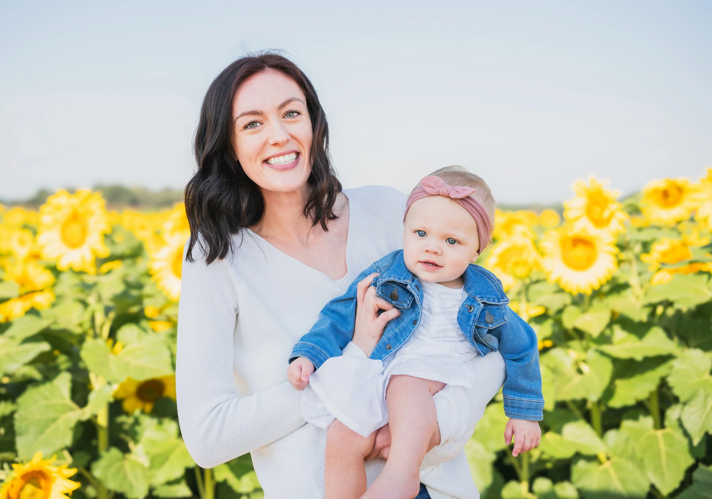 A smiling woman holding a young girl in a sunflower field.