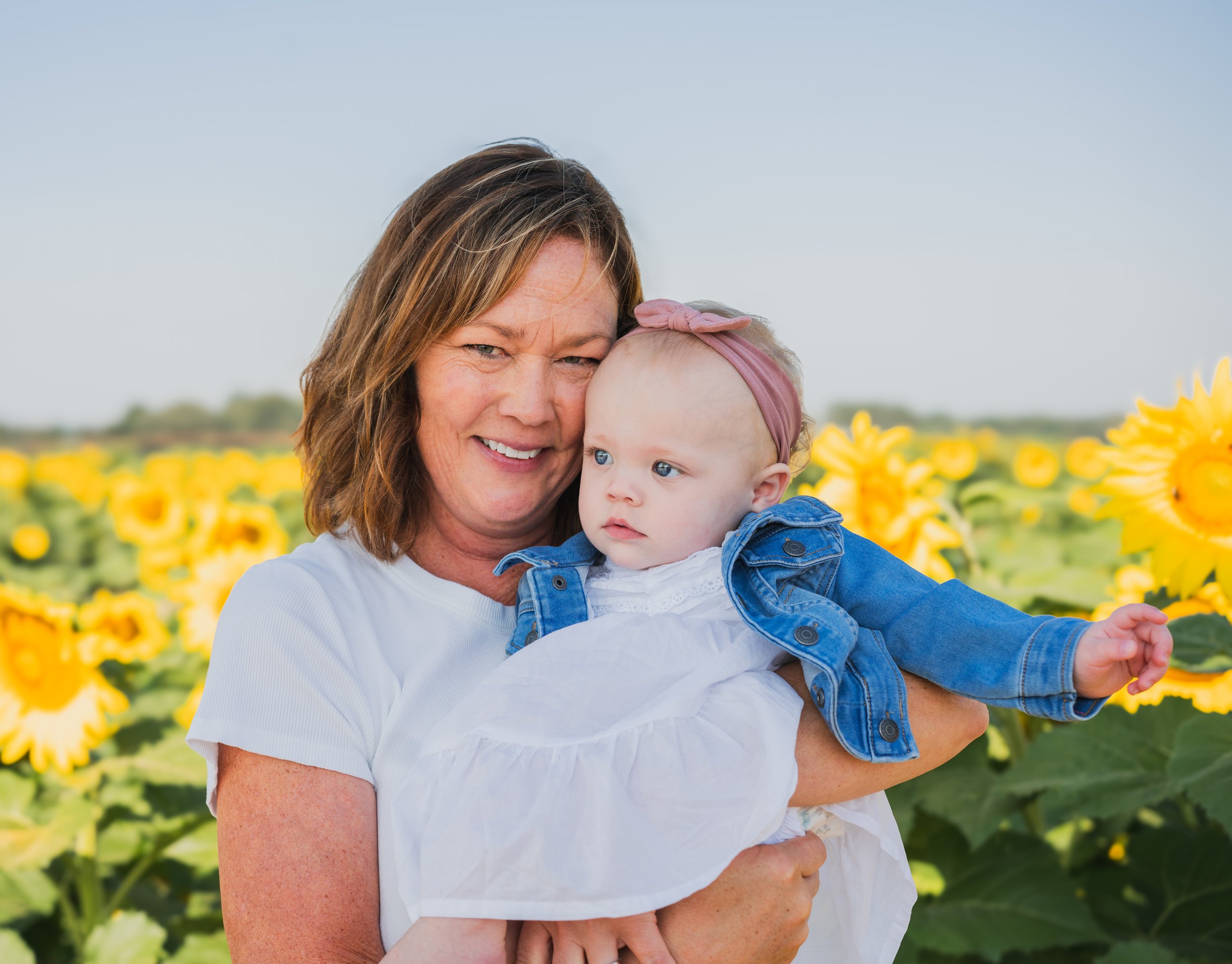 A woman holding a baby girl in a sunflower field.