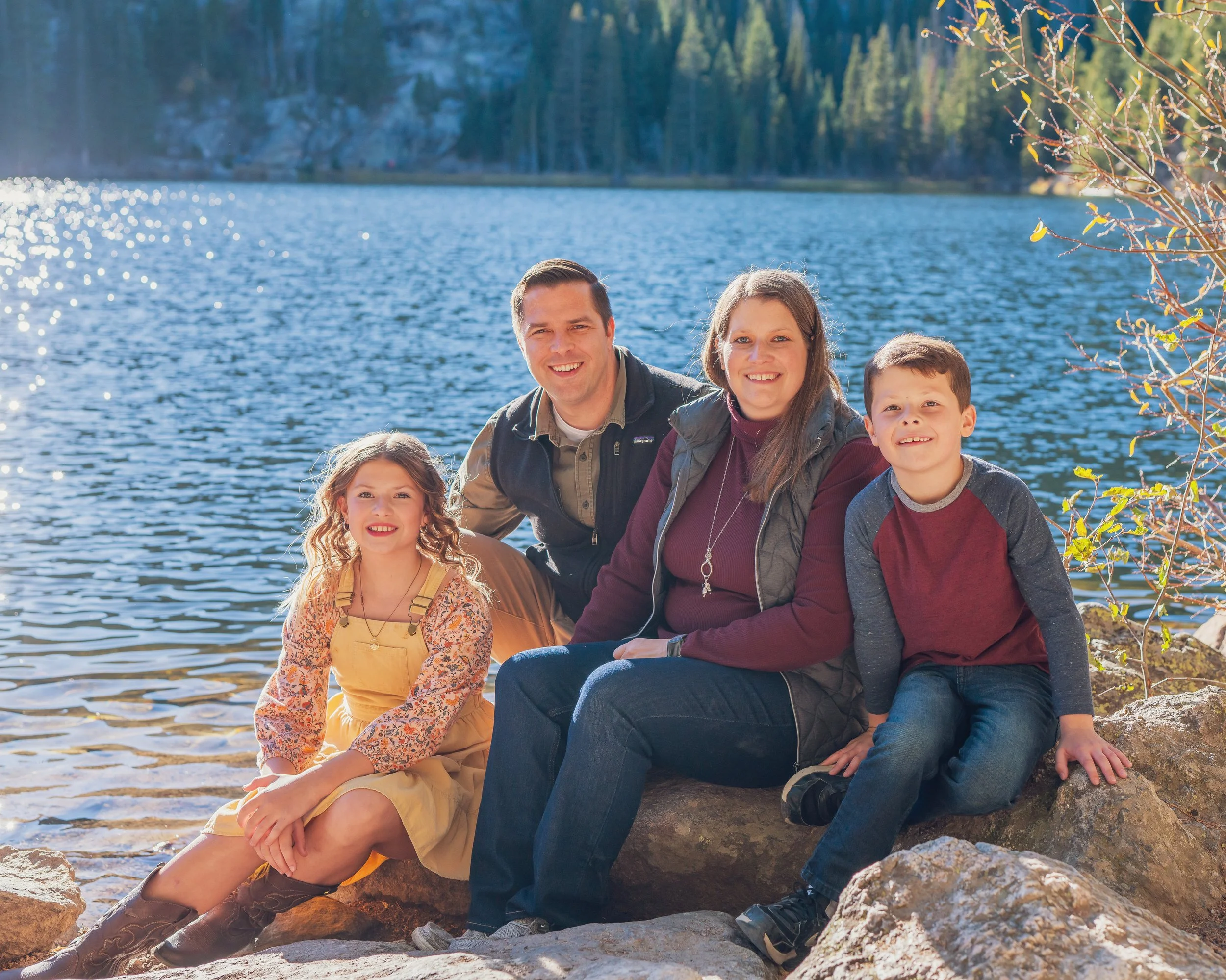 A family of five sitting on rocks by a lake with trees in the background, smiling at the camera.