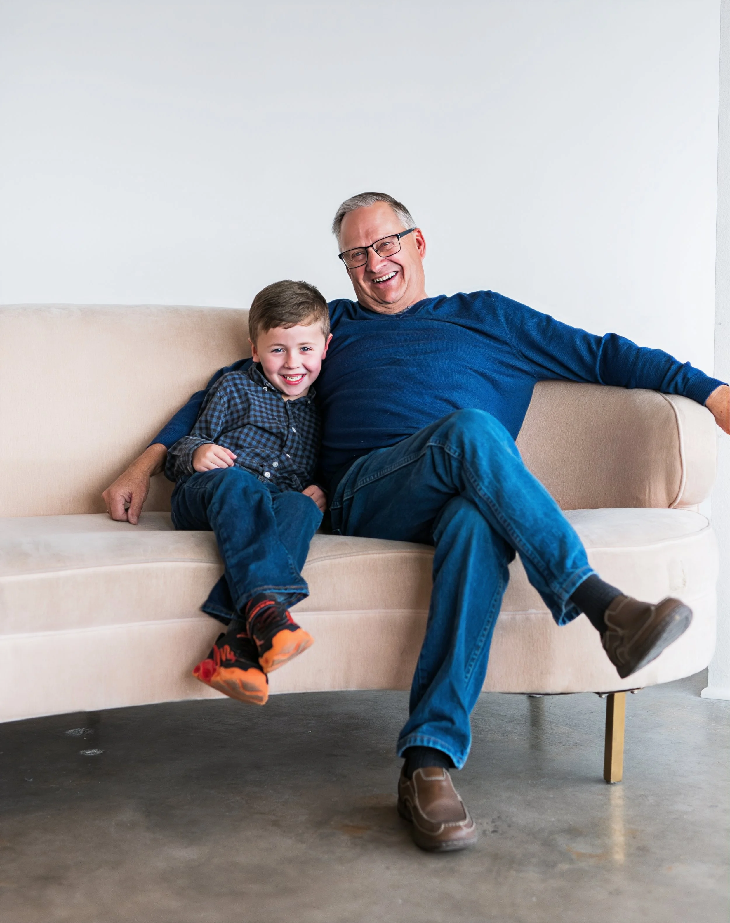 A happy grandfather and young boy sitting on a beige sofa, smiling and enjoying each other's company.