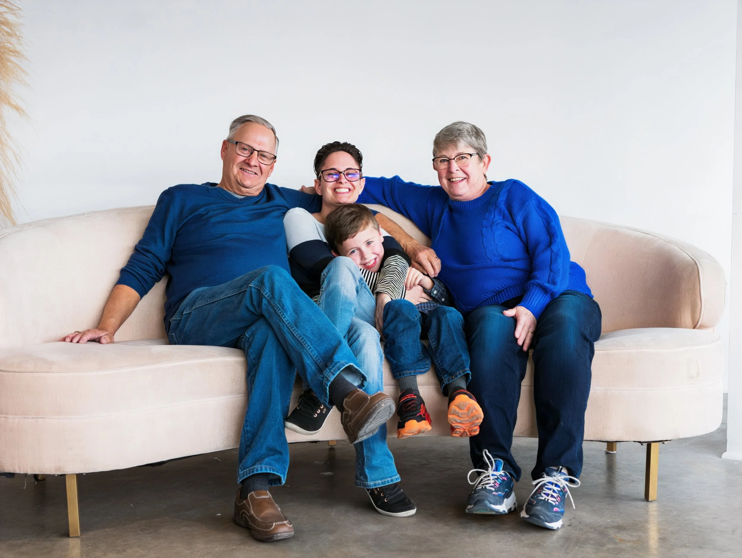 Three generations of family sitting on a beige couch, smiling and enjoying each other's company against a white wall.