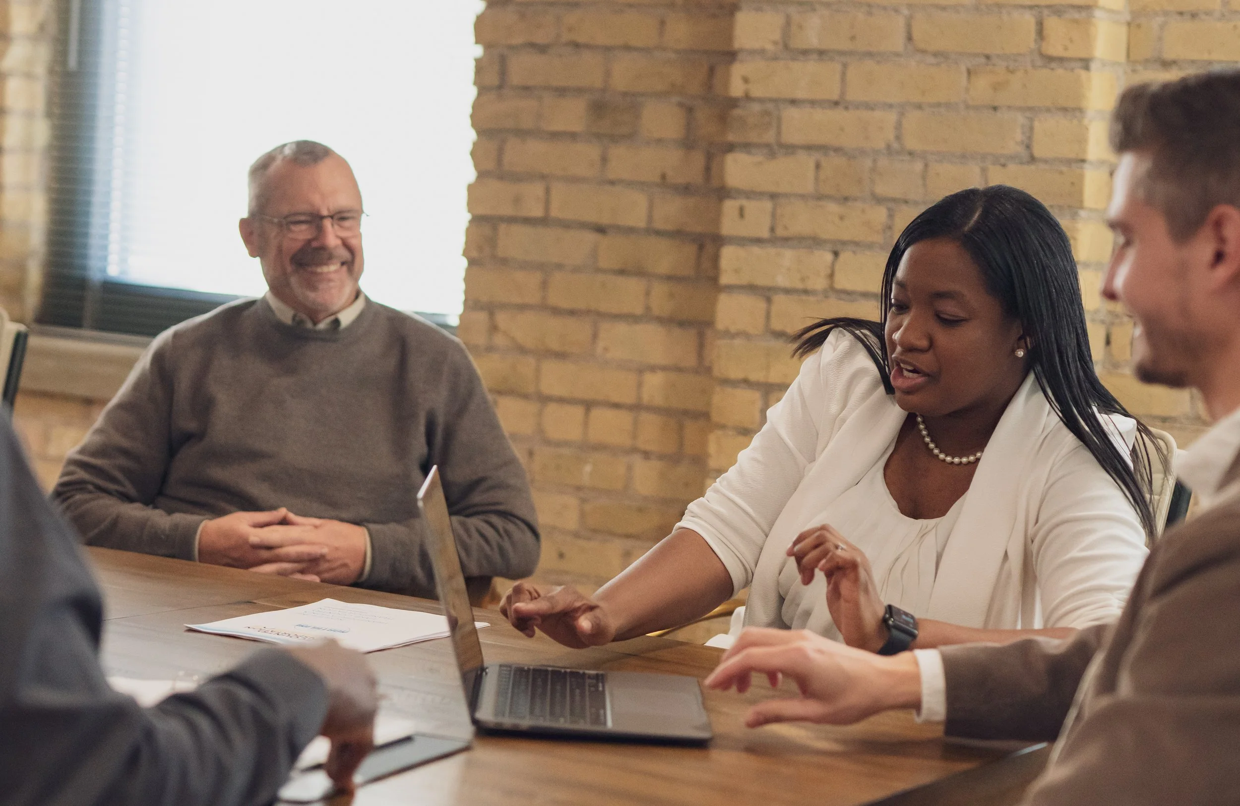 Group of five professionals having a meeting in an office with brick walls, some documents, and laptops on the table.