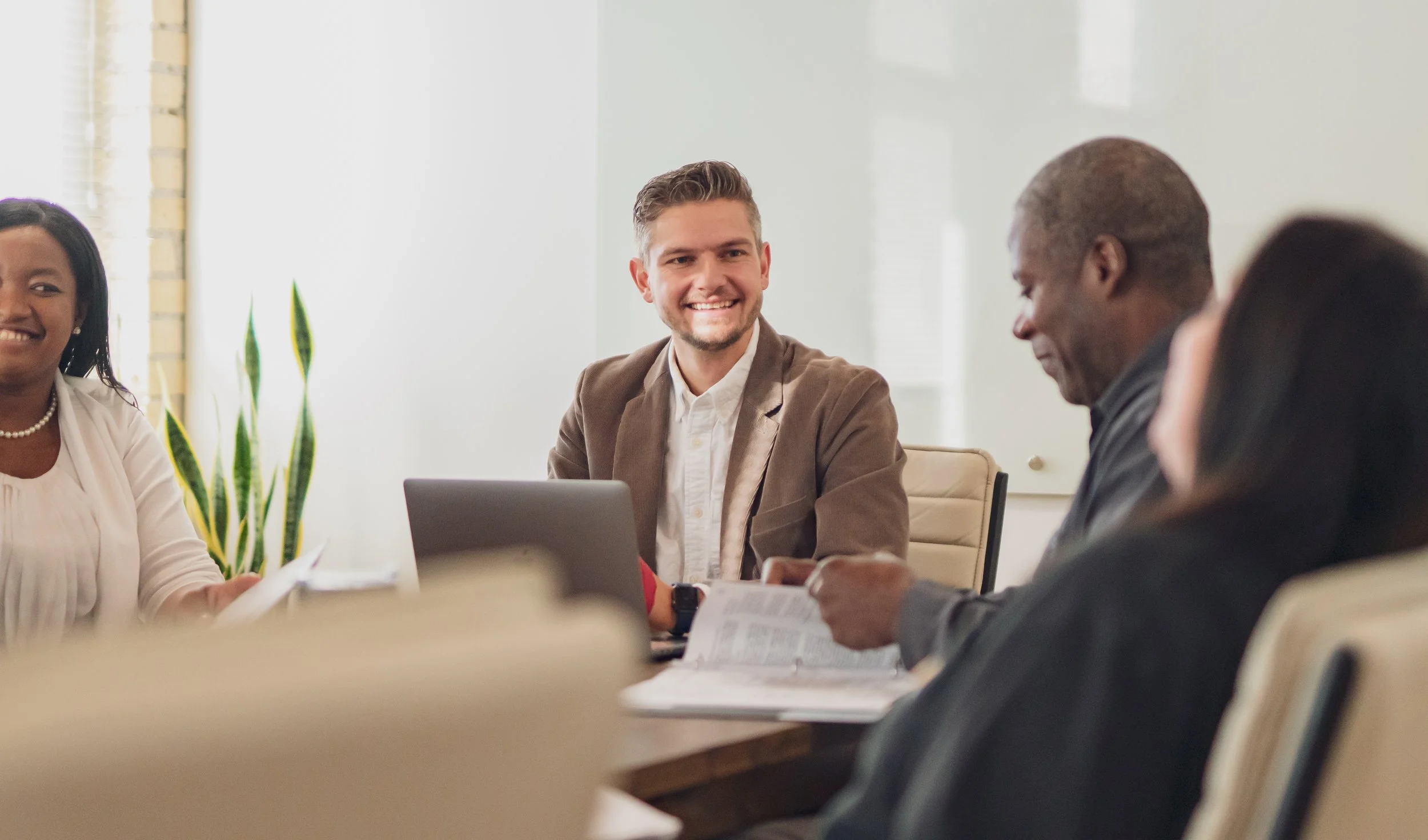 Business meeting with four diverse professionals sitting around a table, engaging and smiling in a modern office