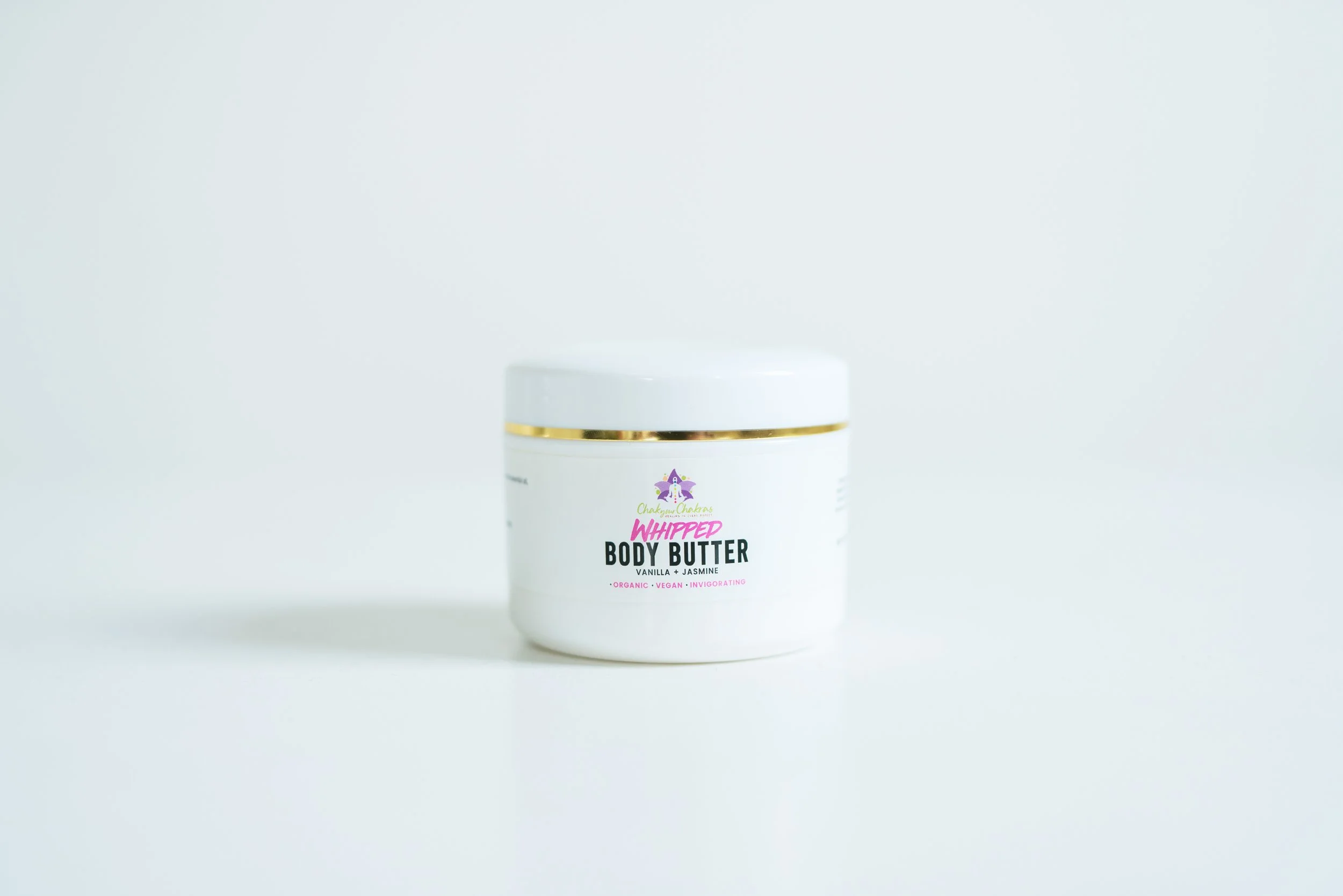 A white container of whipped body butter with a gold band around the lid, labeled as vanilla and jasmine scent, set against a plain white background.